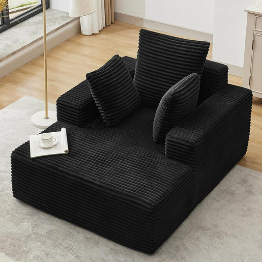 [Black] oversized corduroy chaise lounge chair — angled full view showing deep seat, wide armrests, and three throw pillows
