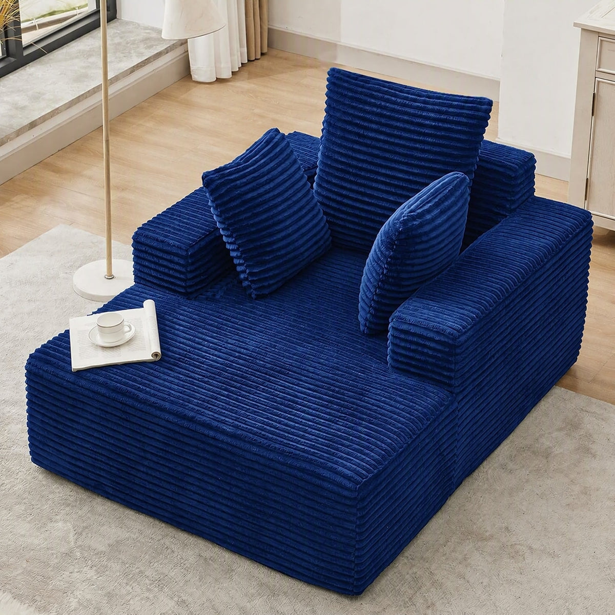 [Blue] oversized corduroy chaise lounge chair, angled full view showing deep seat, wide armrests, and three throw pillows